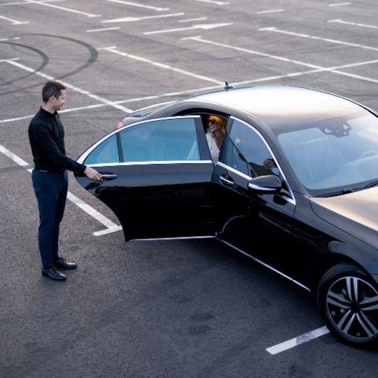 Black Lincoln sedan at airport drop-off with chauffeur assisting passengers, showcasing professional and reliable Ayr Airport Limo service.